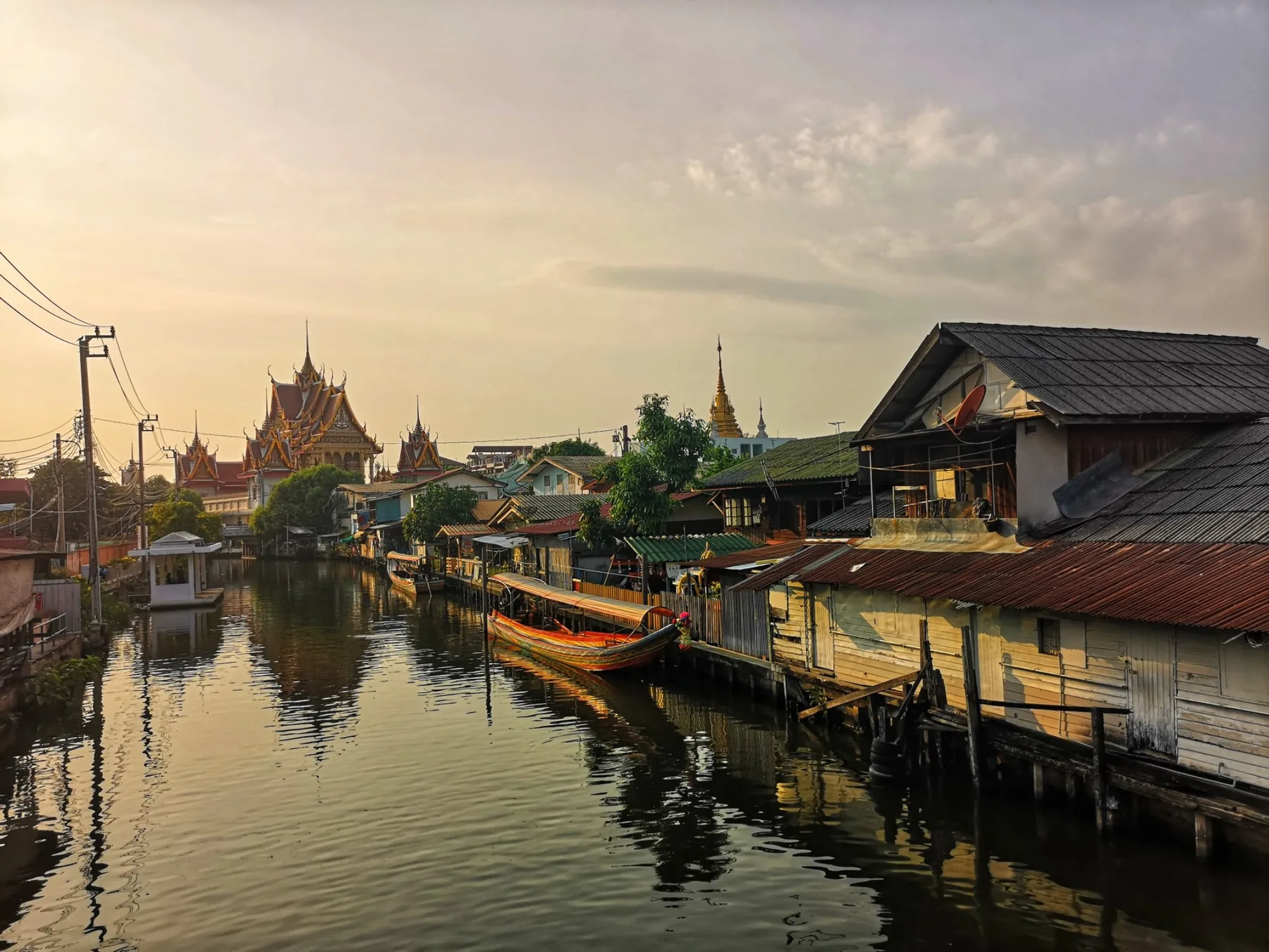 Canal view with longtail boats and temple at sunset