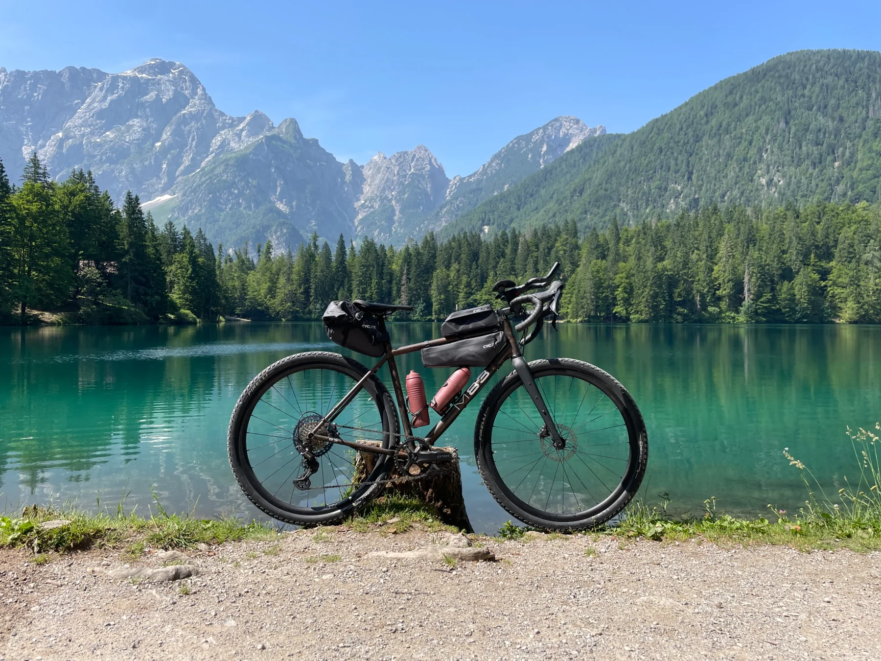 Loaded gravel bike in front of a clear alpine lake and mountains