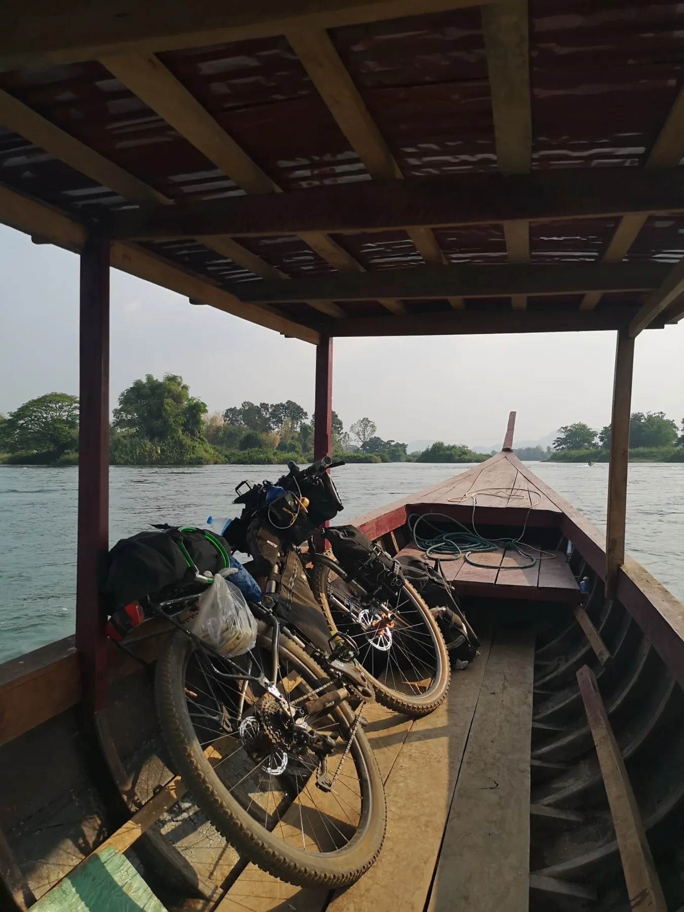 Bikepacking bicycle and outdoor gear on a wooden boat during a river crossing