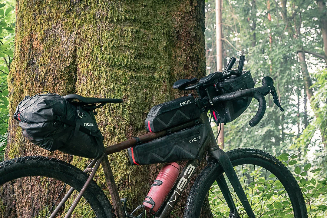 Loaded gravel bike with black bikepacking bags in a forest