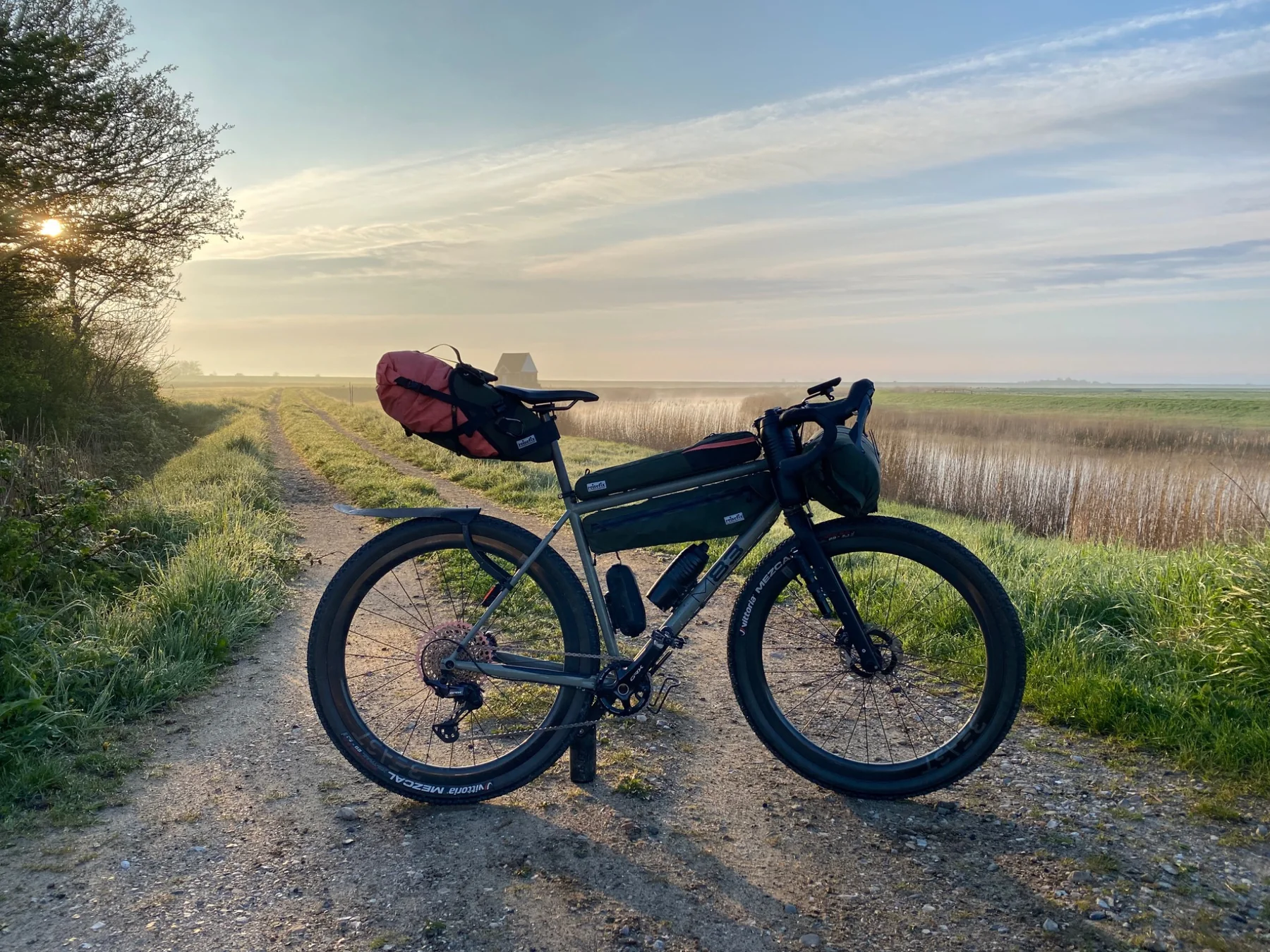 Loaded gravel bike on a track near wetlands at golden hour