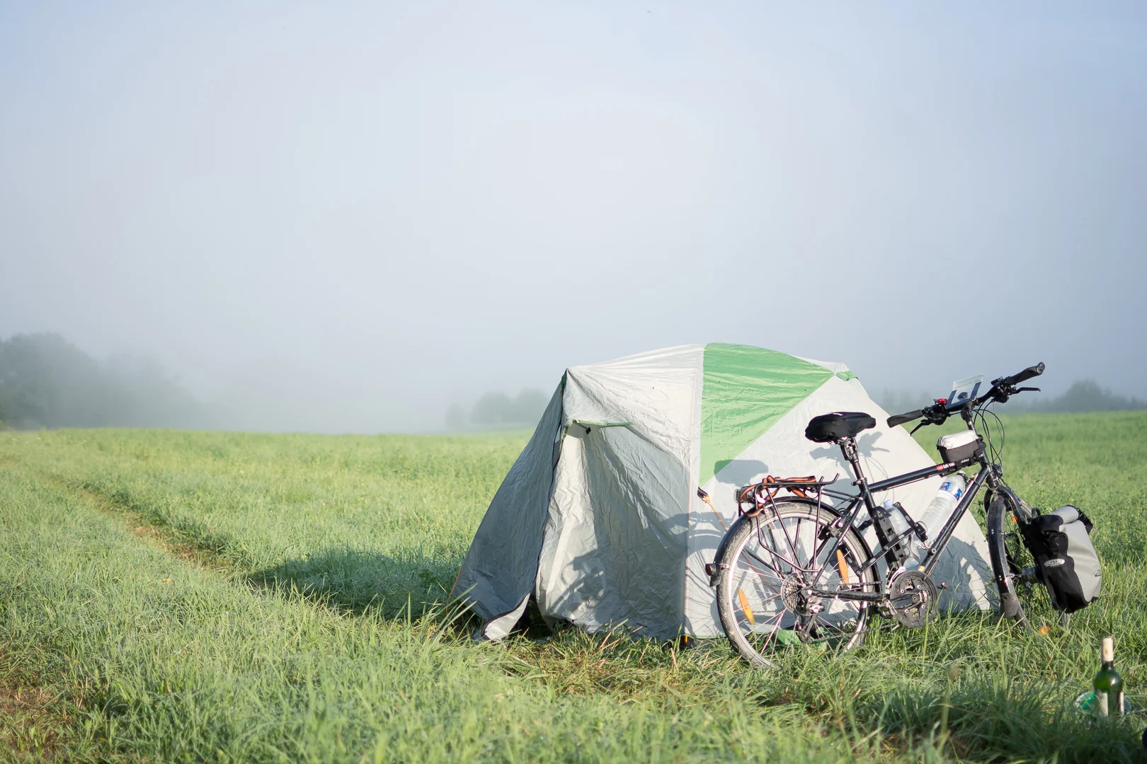 Tent and bicycle in a foggy field at sunrise